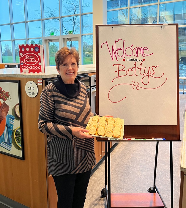 Jackie Sheehan posing with her Spiced Pumpkin Cookies in front of a sign that says “Welcome Home Bettys”