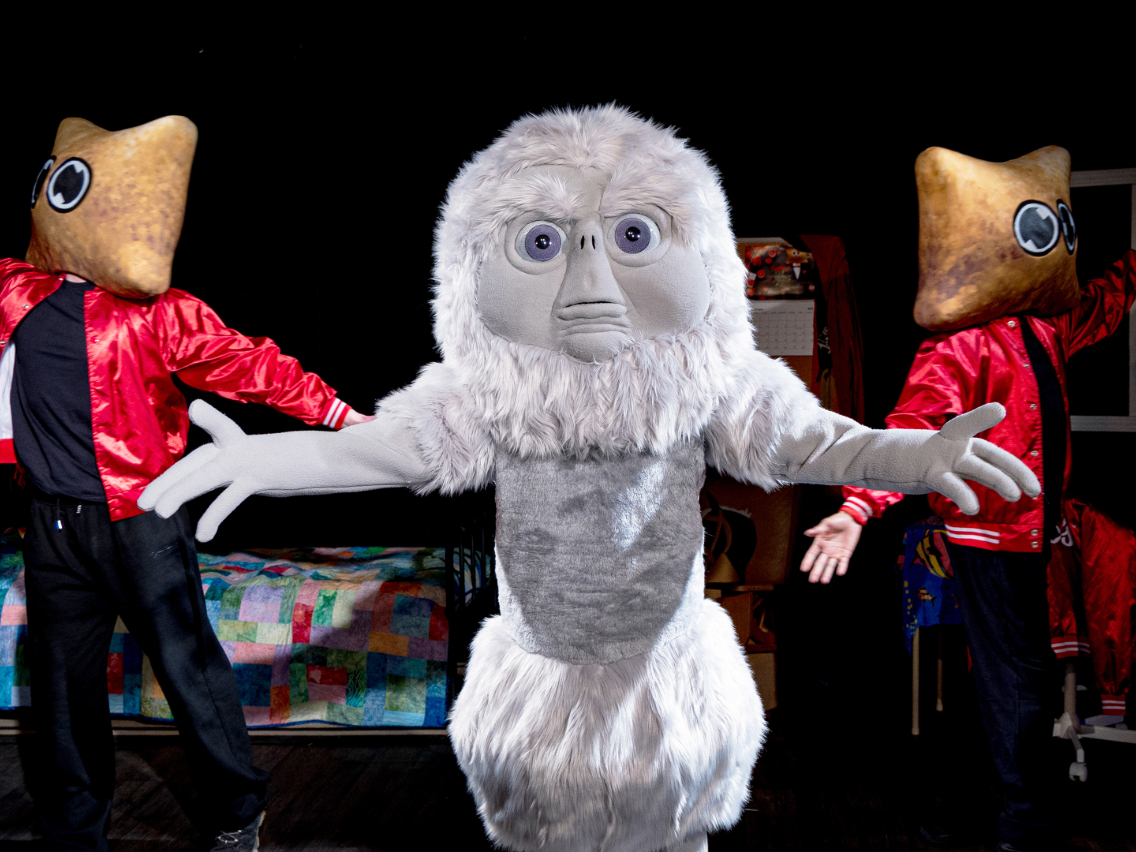 ​Intergalactic friend Chazmo stands center stage singing about his love for Totino‘s Pizza Rolls with outstretched arms while two backup dancers dressed as pizza rolls dance on either side in a dark, theatrical setting. 